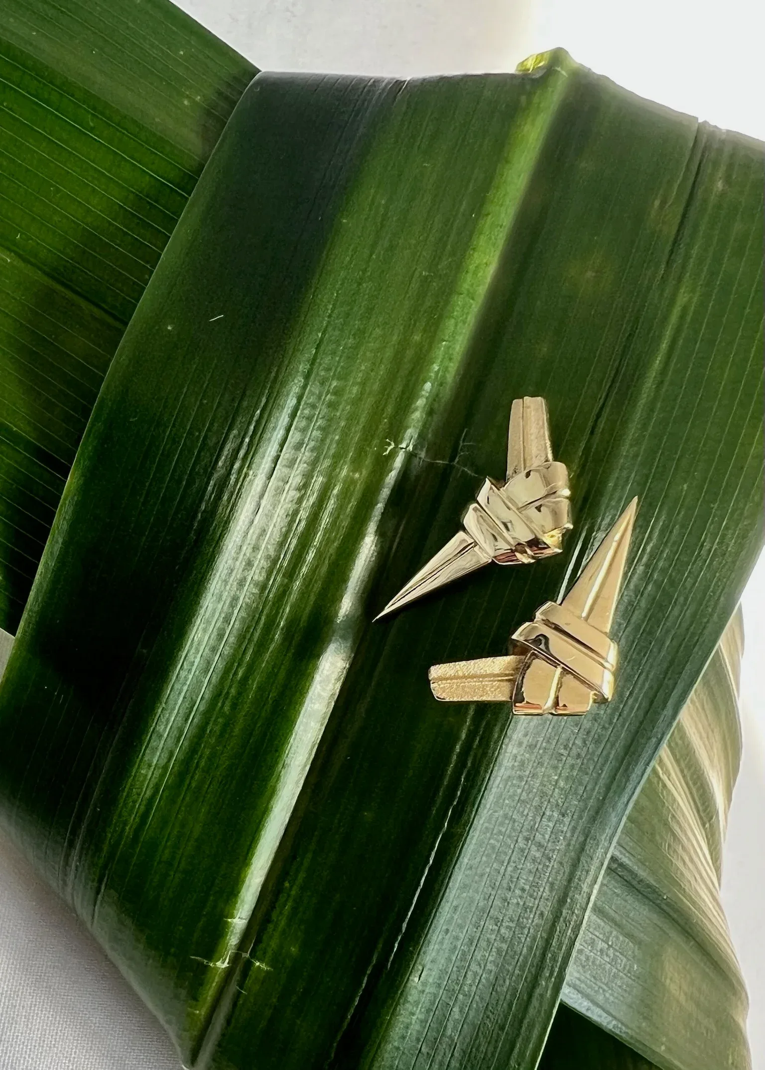 Two gold cone-shaped earrings displayed on green banana leaves