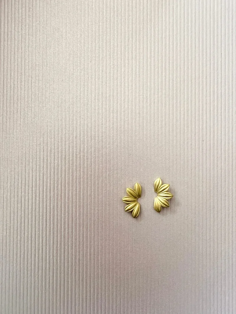 Pair of gold leaf-shaped earrings on textured beige background