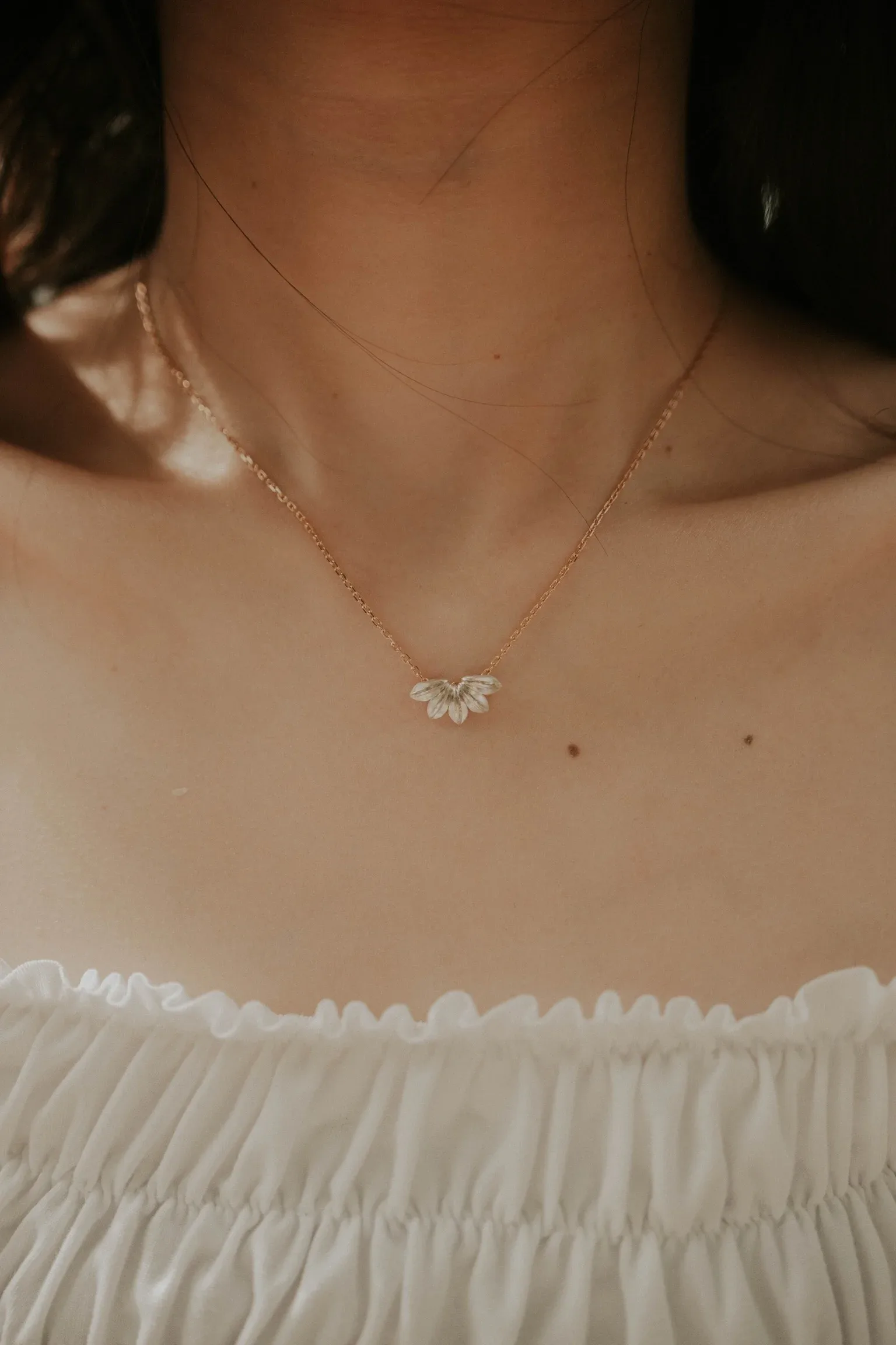Woman wearing rose gold delicate necklace with leaf-shaped pendant, white off-shoulder top