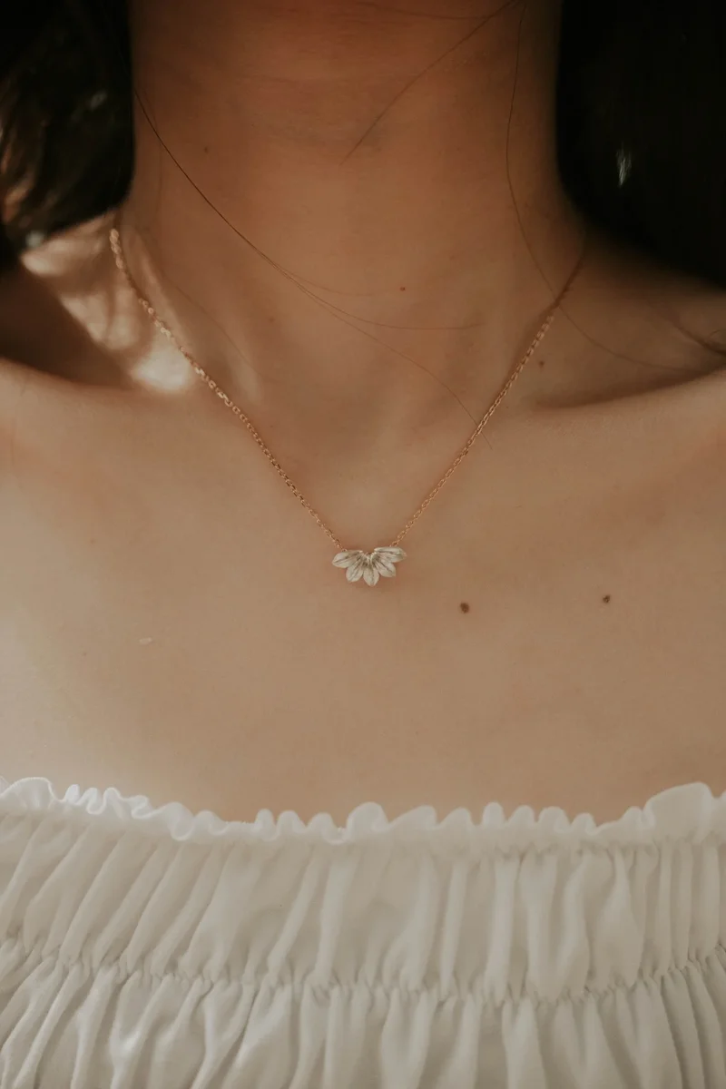 Woman wearing rose gold delicate necklace with leaf-shaped pendant, white off-shoulder top