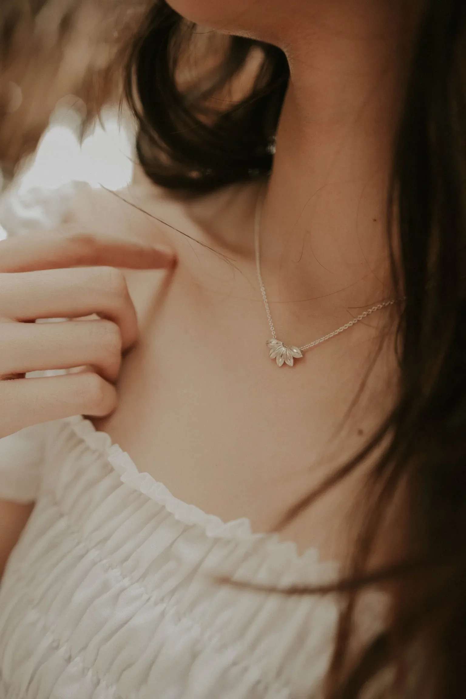 Woman wearing silver daisy pendant necklace with white ribbed top