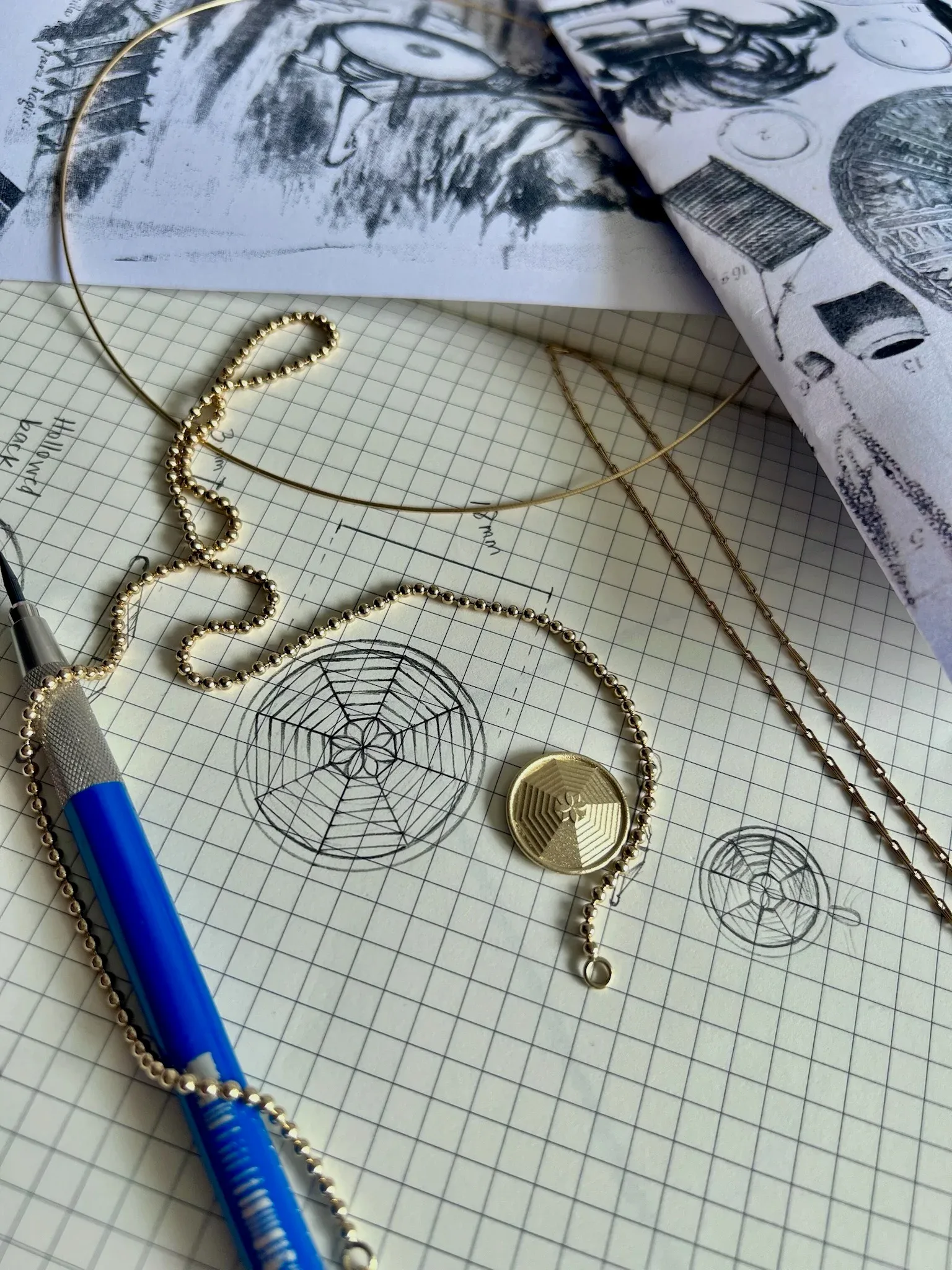 Gold beaded necklace with circular pendant displayed on graph paper with sketches, blue pen, and design references