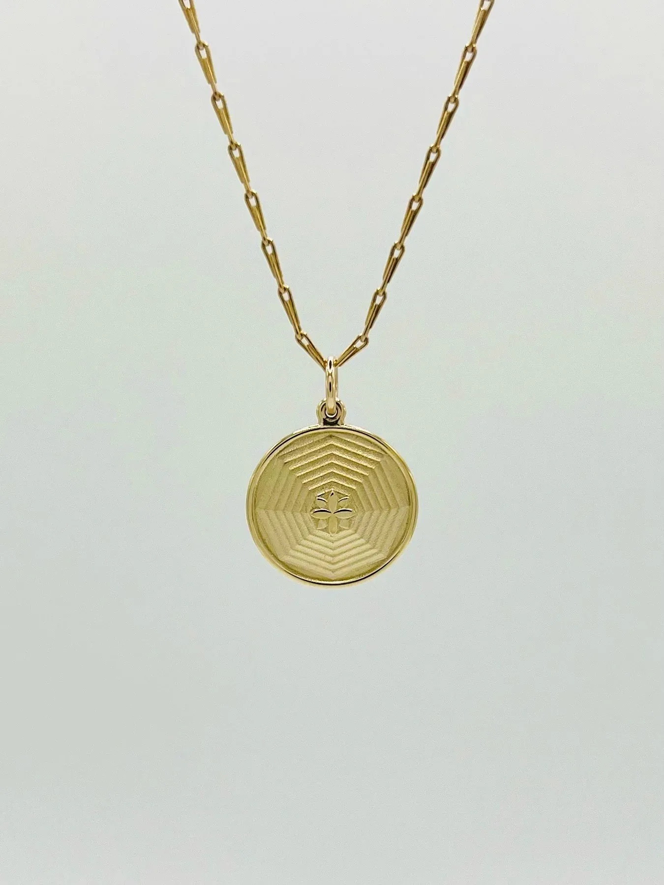 Gold circular pendant necklace with concentric line pattern and small cross motif in center