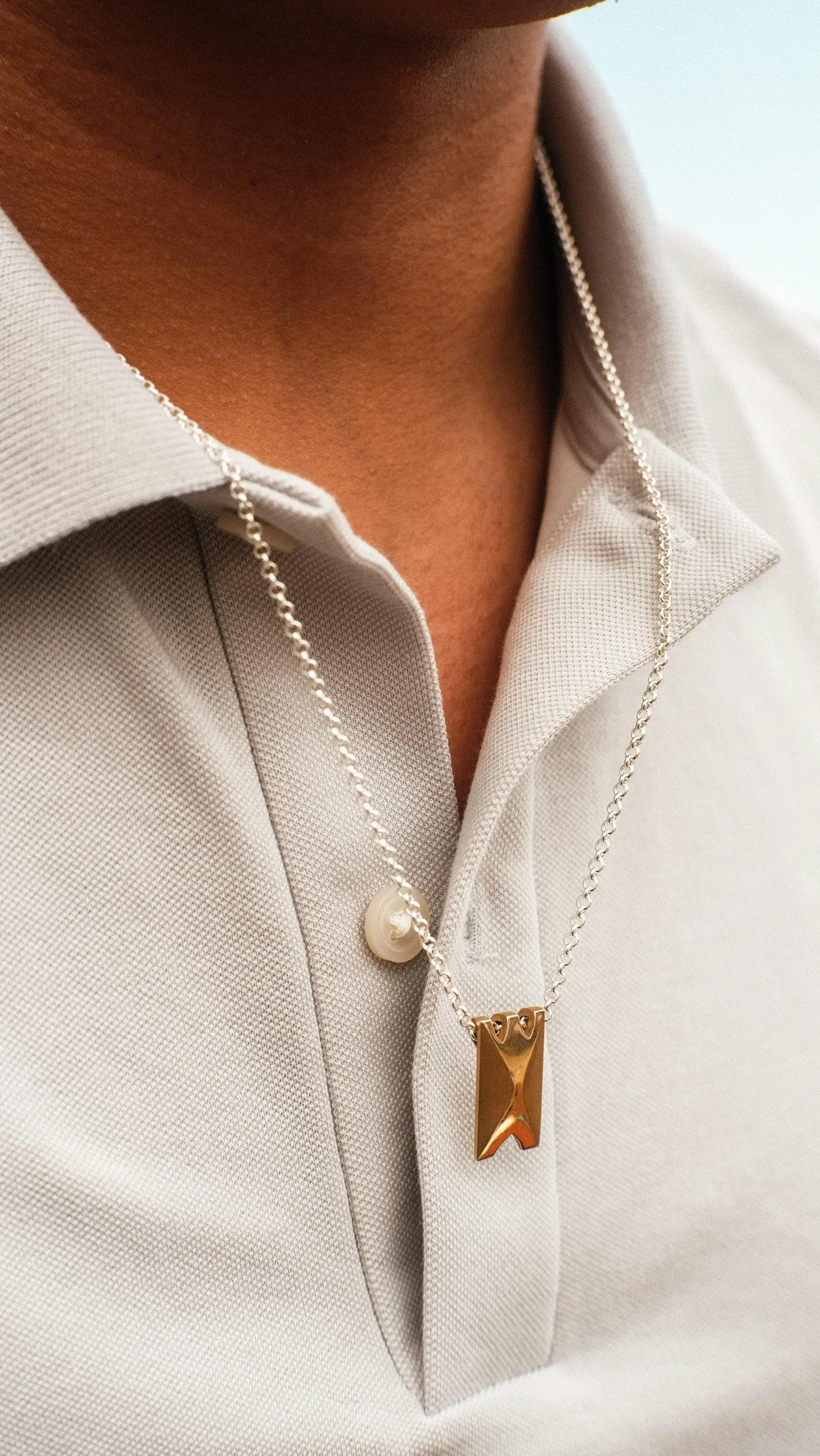 Person wearing cream linen shirt with silver chain necklace featuring gold rectangular pendant and pearl charm