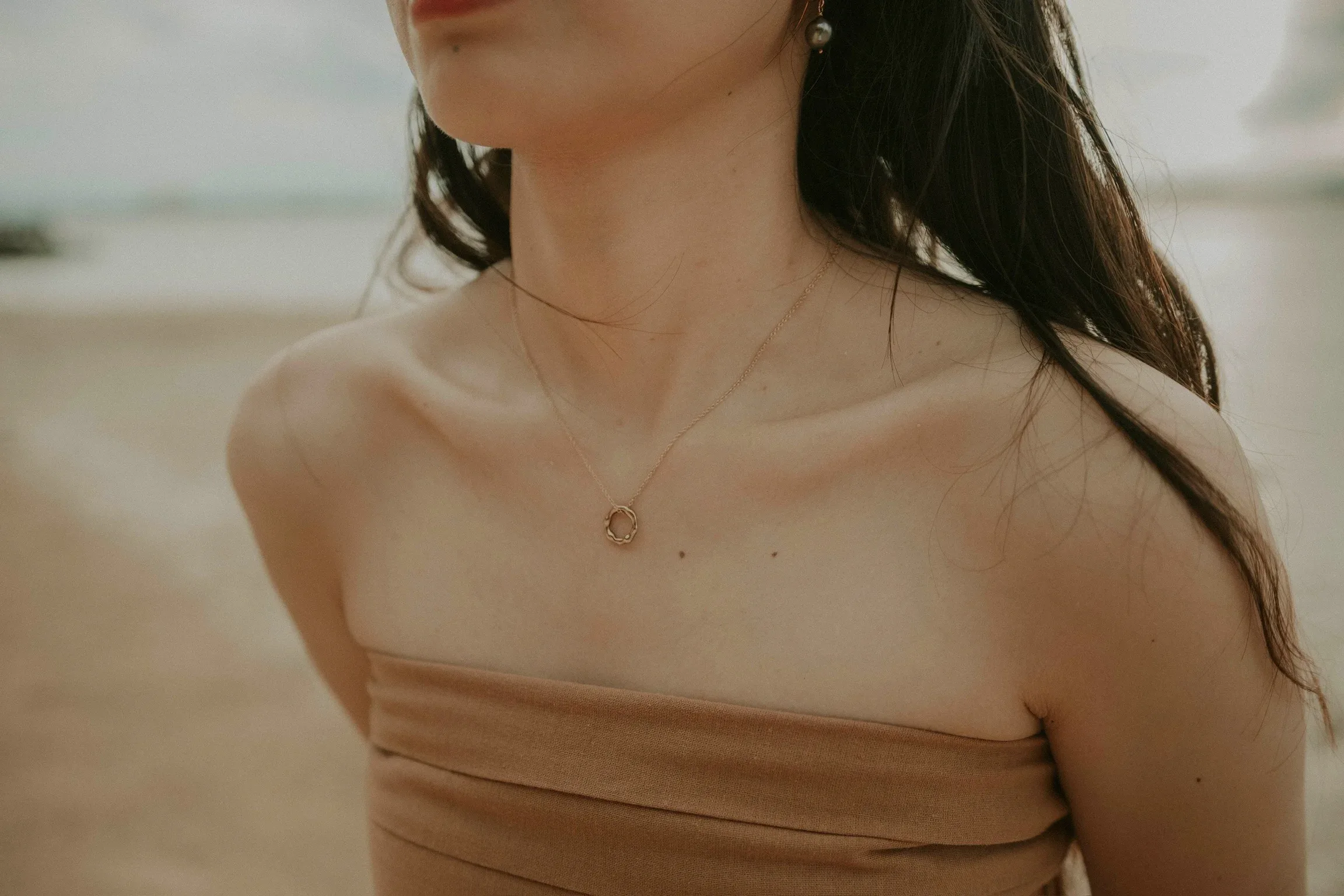 Woman wearing gold circular pendant necklace on beach with long dark hair