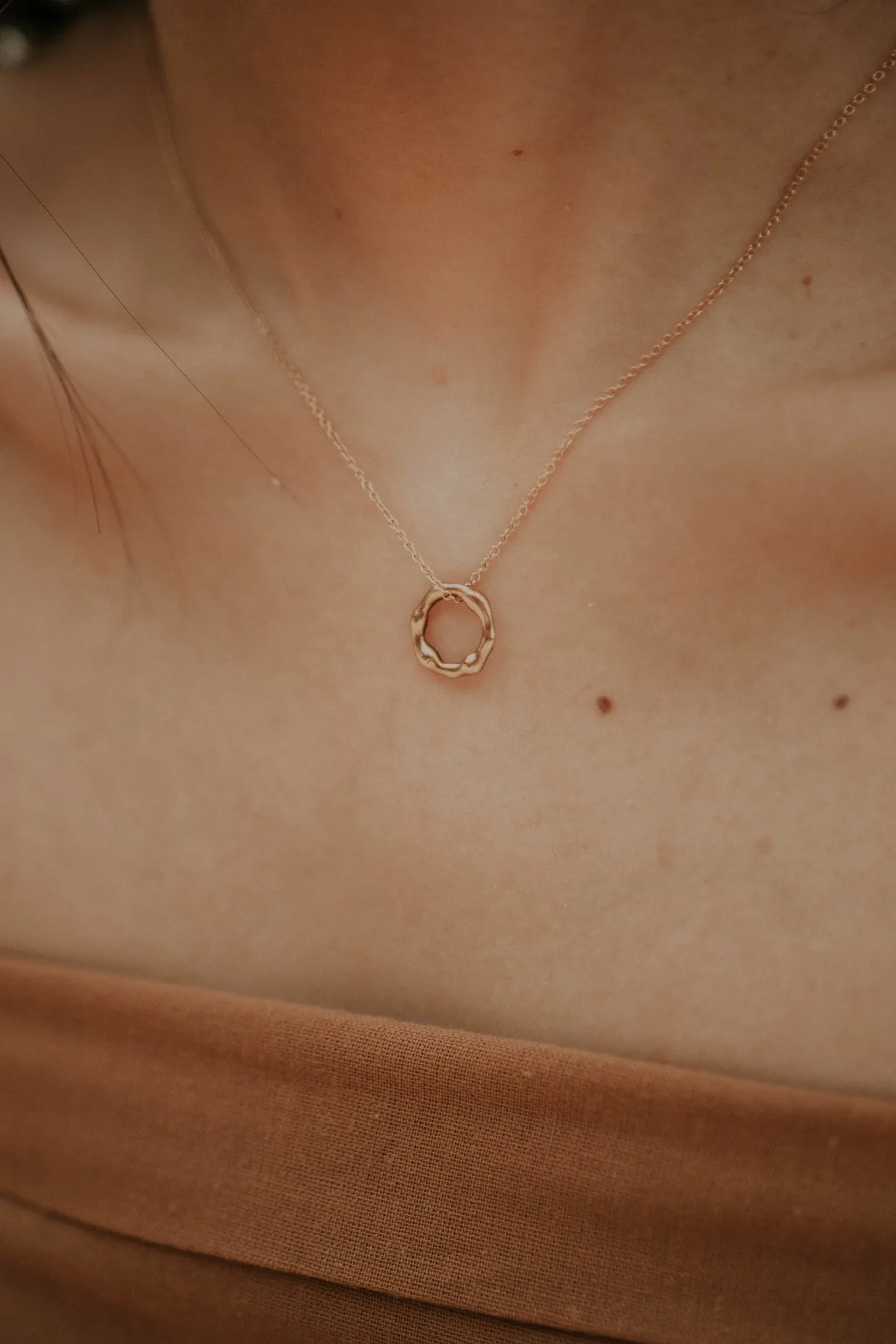 Rose gold necklace with small circular textured pendant worn on person's chest