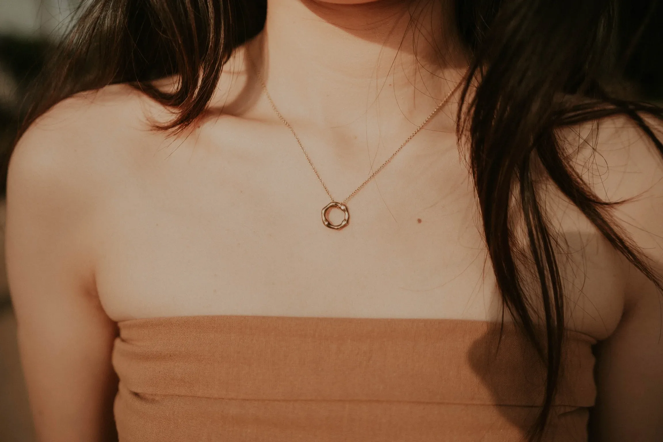 Woman wearing rose gold circle pendant necklace with beige strapless top