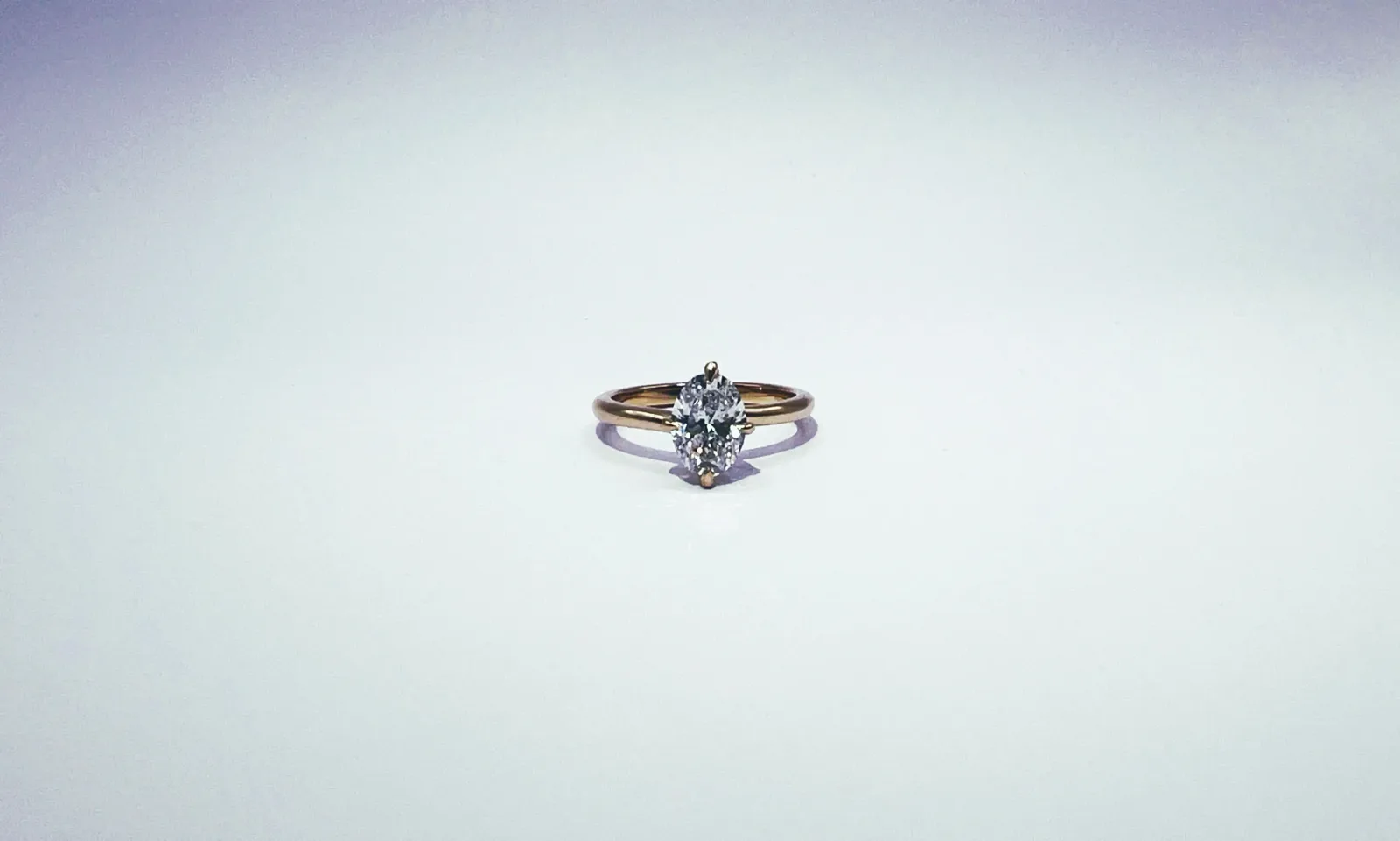 Diamond solitaire engagement ring with oval-cut stone in gold band on white background