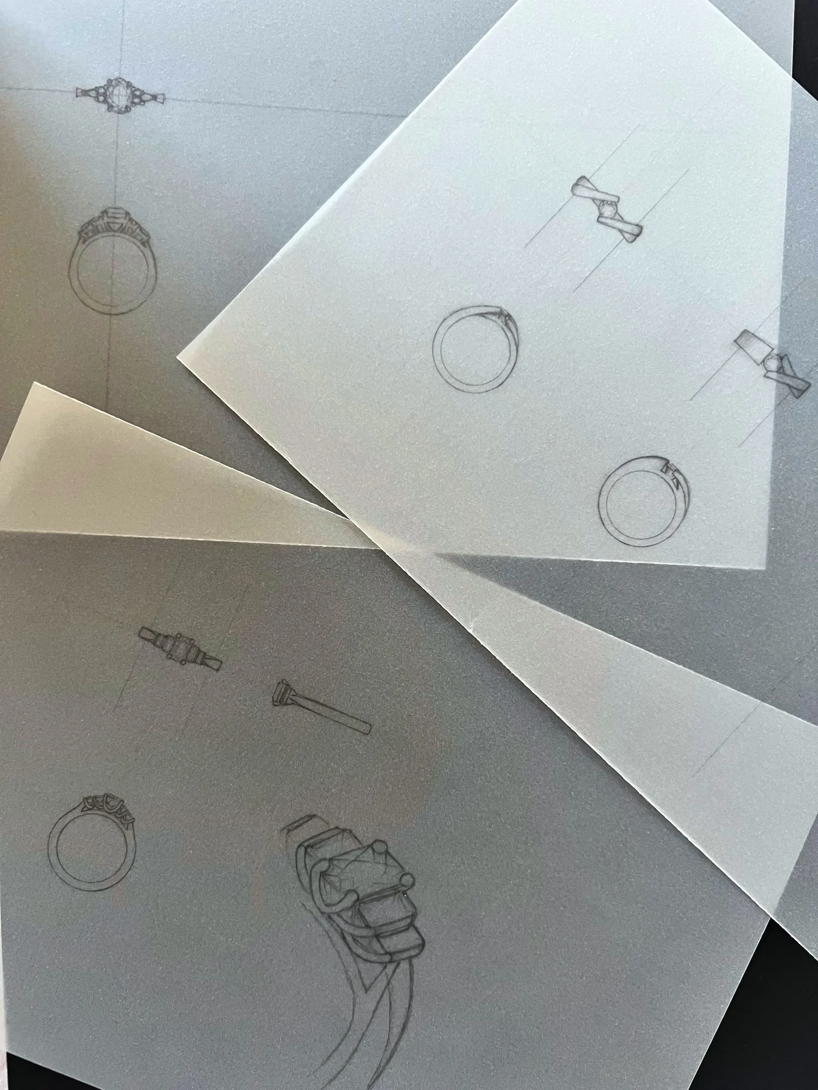 Sketches and design drawings of jewelry pieces including rings, earrings, and brooches on white and grey paper